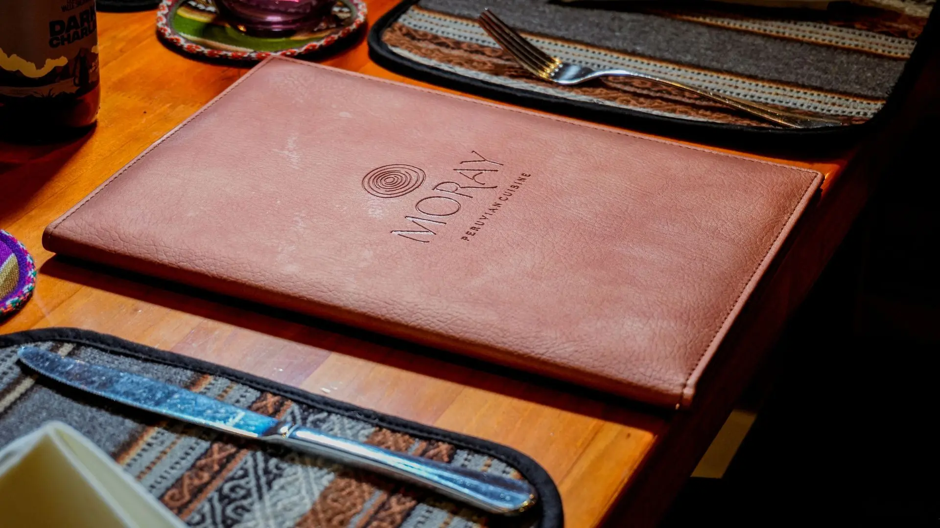 Leather menu of Moray Peruvian Cuisine on a table with Andean textile, Cusco